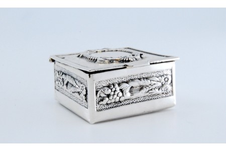 Caixa de comprimidos em prata com laços e relevos na envolvência com tampa basculante.